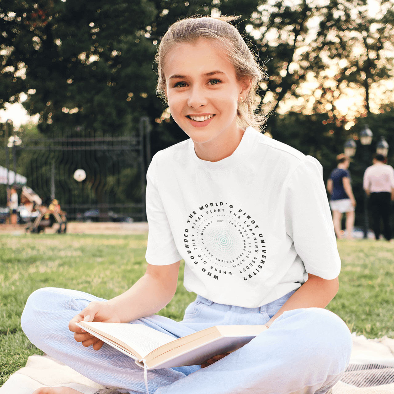 Girl sitting on picnic rug wearing T-Shirt with oldest University Question printed.